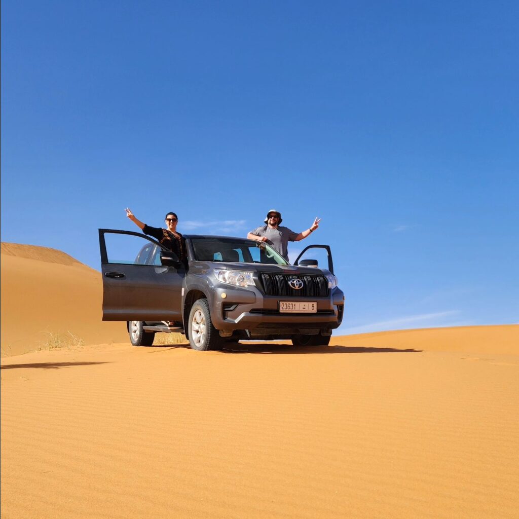 Two people in a jeep on sand dunes in the desert