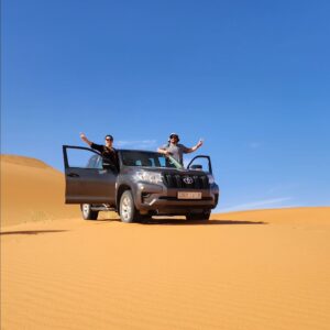 Two people in a jeep on sand dunes in the desert